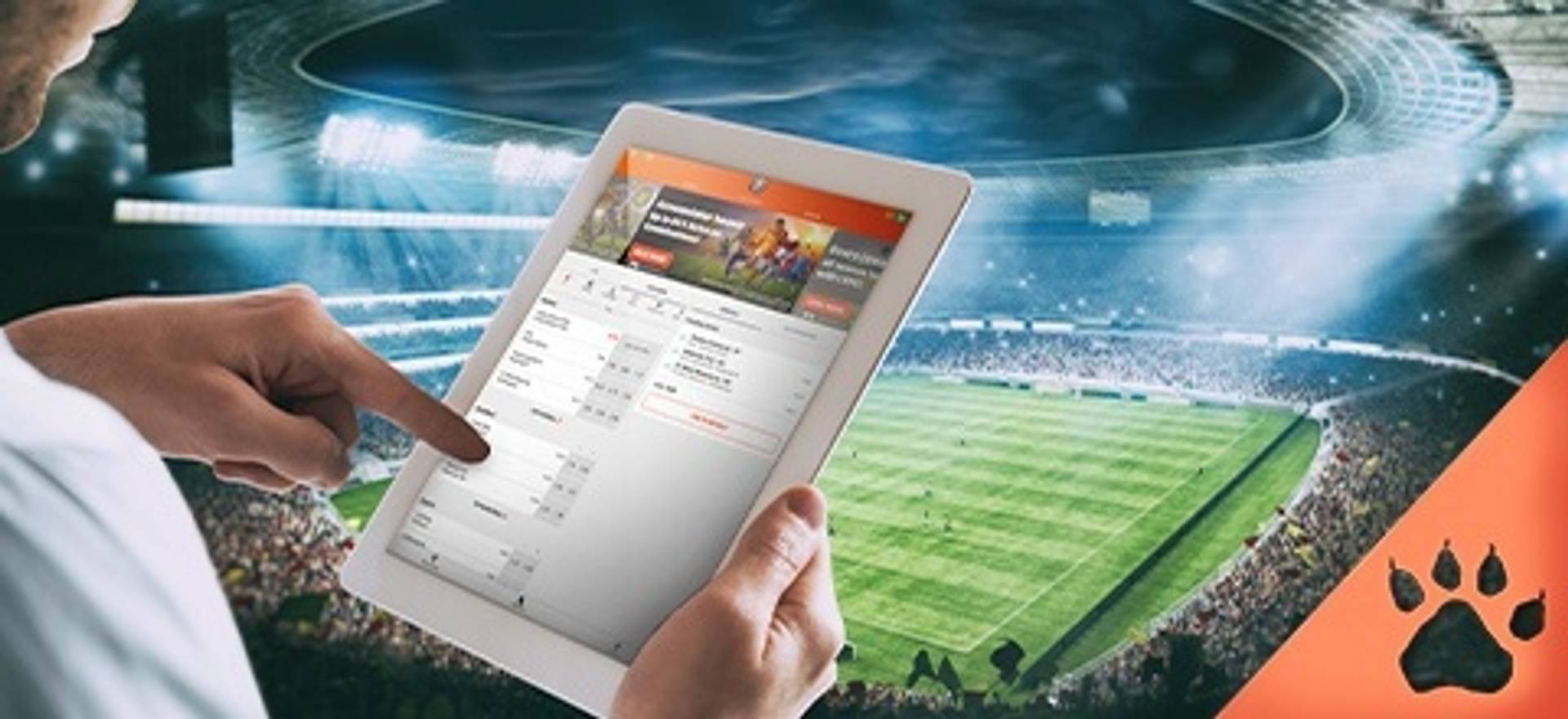 Persona usando una tableta para apostar en un partido deportivo; estadio de fútbol de fondo.